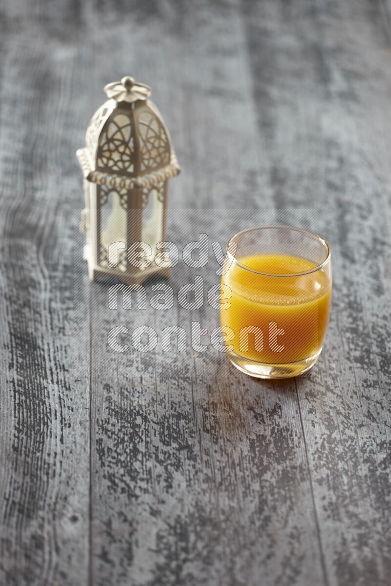 A white lantern with different drinks, dates, nuts, prayer beads and quran on grey wooden background