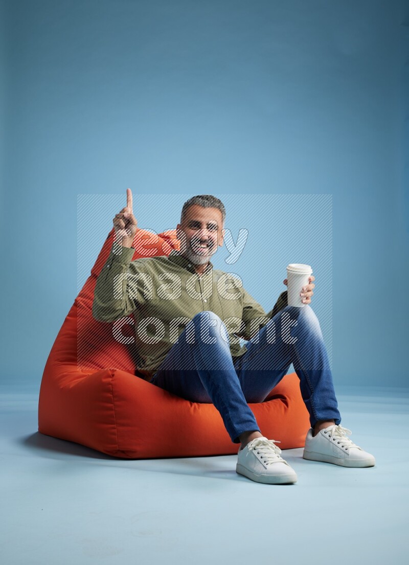 A man sitting on an orange beanbag and drinking coffee