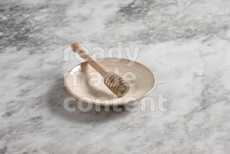Beige pottery plate with wooden honey dipper in it on grey marble background