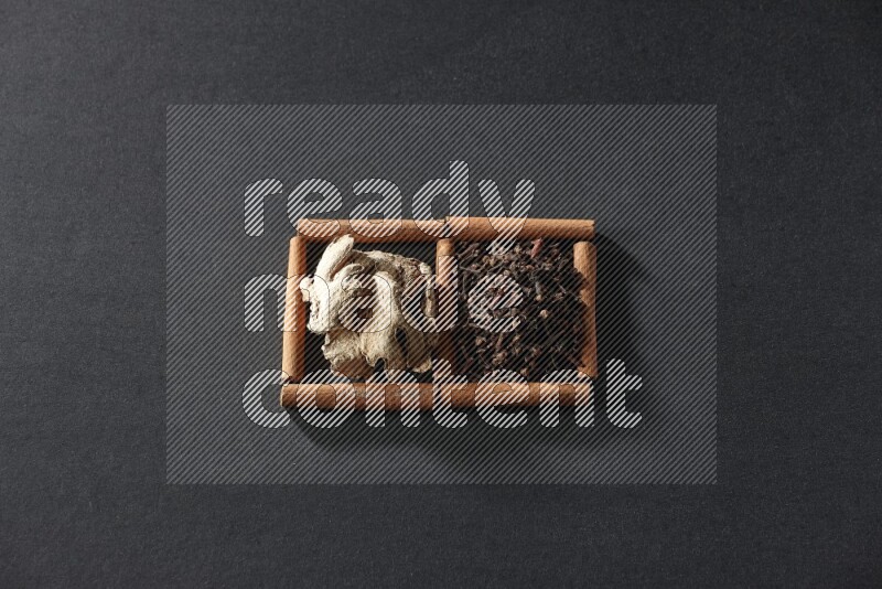 2 squares of cinnamon sticks full of cloves and dried ginger on black flooring