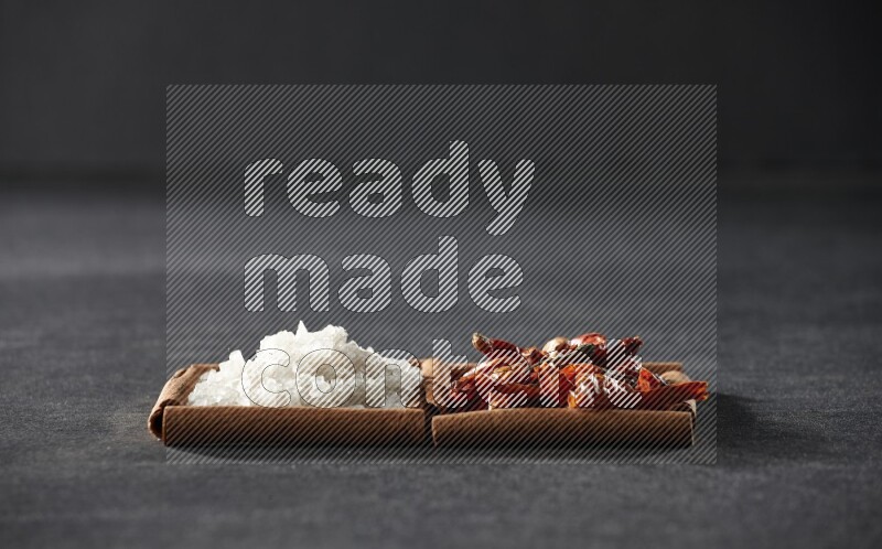 2 squares of cinnamon sticks full of chilis and salt on black flooring