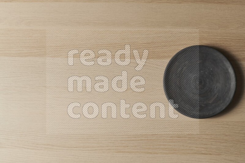 A circular black pottery plate on light wooden background