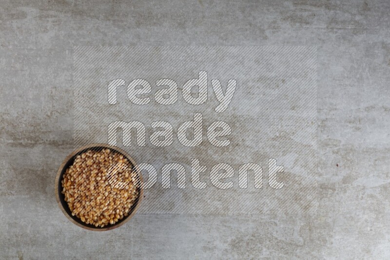 corn kernel in a wooden bowl on a grey textured countertop