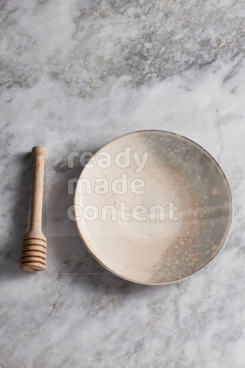 Multicolored pottery plate with wooden honey dipper on the side on grey marble background