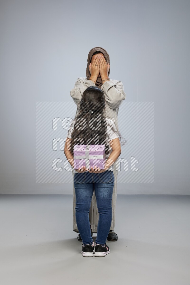 A girl standing hiding a gift behind her back for her mother on gray background