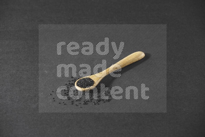 A wooden spoon full of black seeds and seeds spread beside it on a black flooring