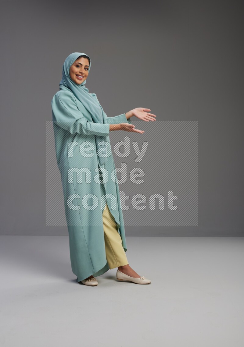 Saudi Woman wearing Abaya standing interacting with the camera on Gray background