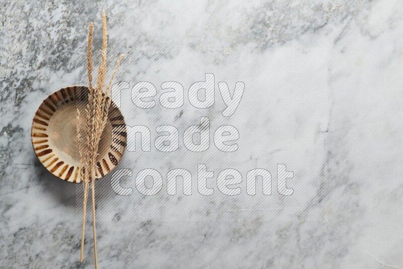 Wheat stalks on multicolored pottery plate on grey marble background