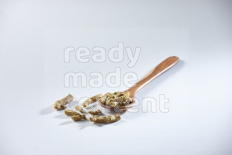 A wooden ladle full of dried turmeric fingers on white flooring