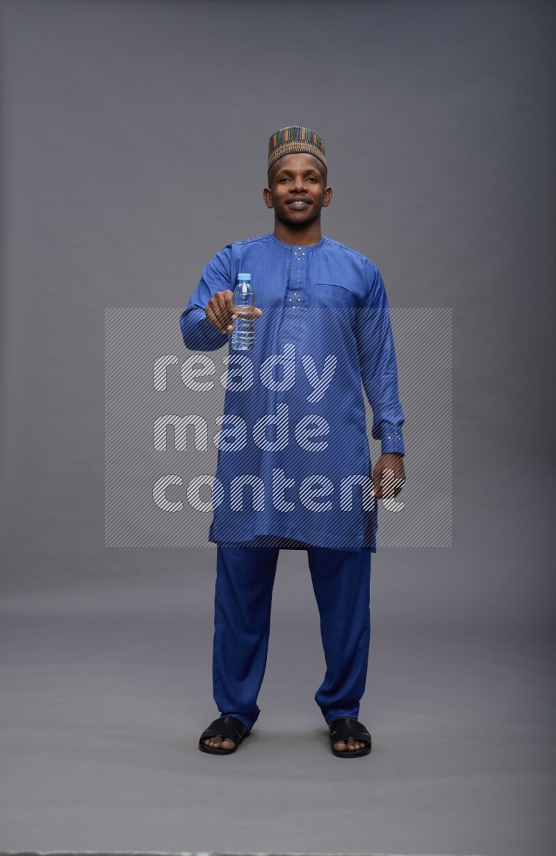 Man wearing Nigerian outfit standing drinking water on gray background
