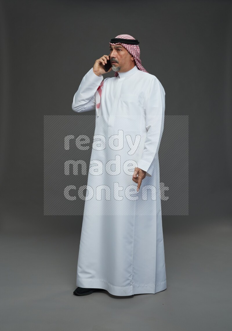 Saudi man with shomag Standing talking on phone on gray background