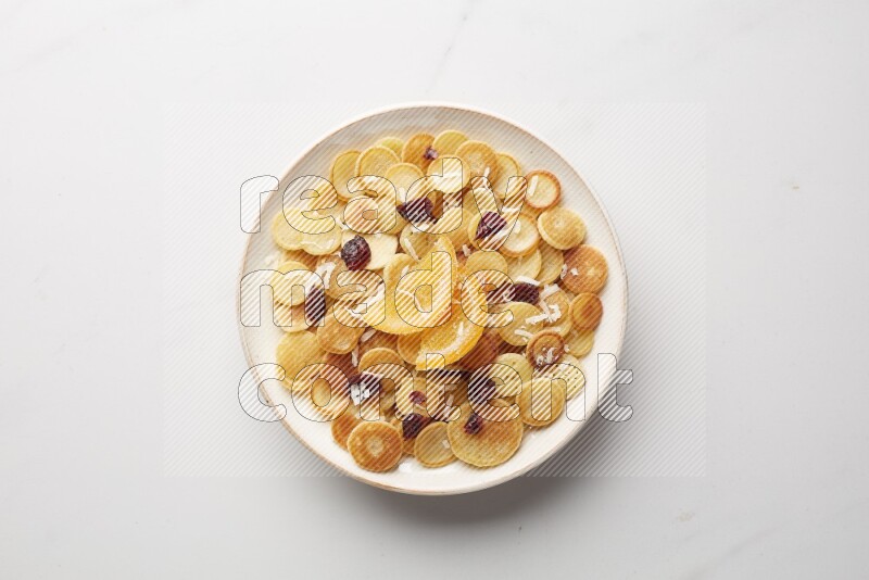 Top-view shot of orange candy cereal pancakes in a round bowl on white background