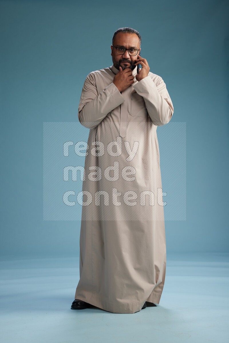 Saudi Man without shimag Standing talking on phone on blue background