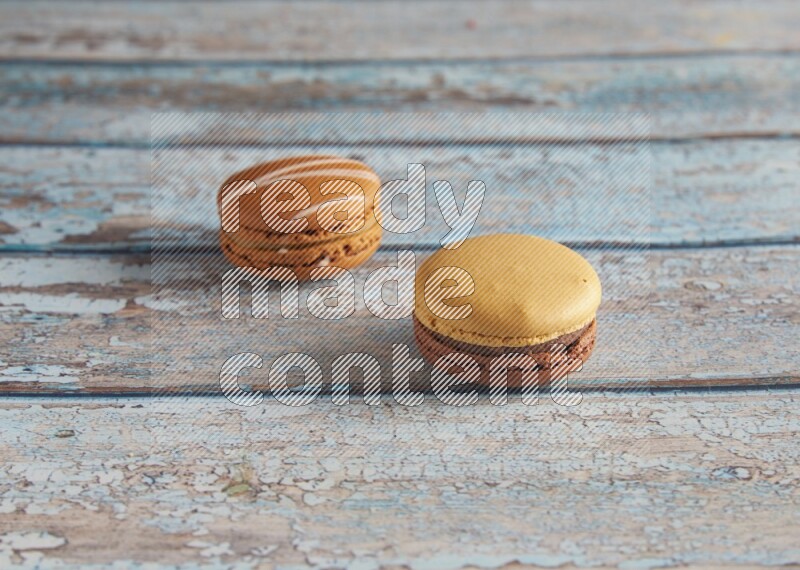 45º Shot of of two assorted Brown Irish Cream, and Yellow, and Brown Chai Latte macarons  on light blue background
