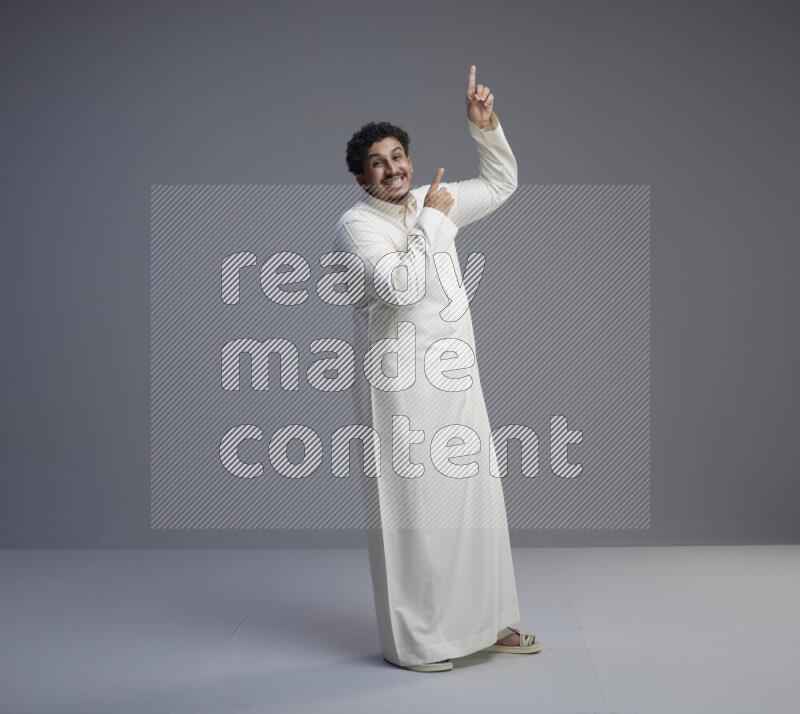 A Saudi man standing wearing thob interacting with the camera on gray background