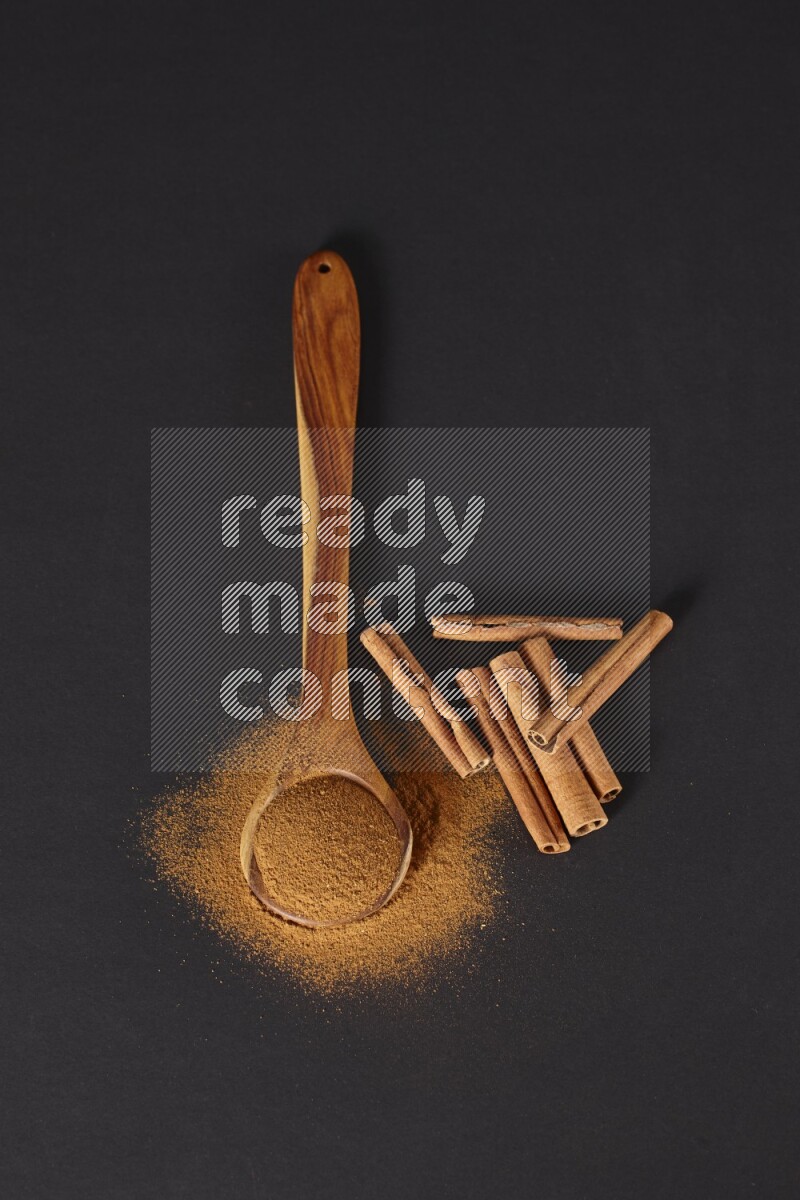Cinnamon powder in a spoon ladle and spreaded on the floor beside it cinnamon sticks on the floor on black background in different angles