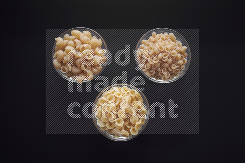 Different pasta types in glass bowls on black background