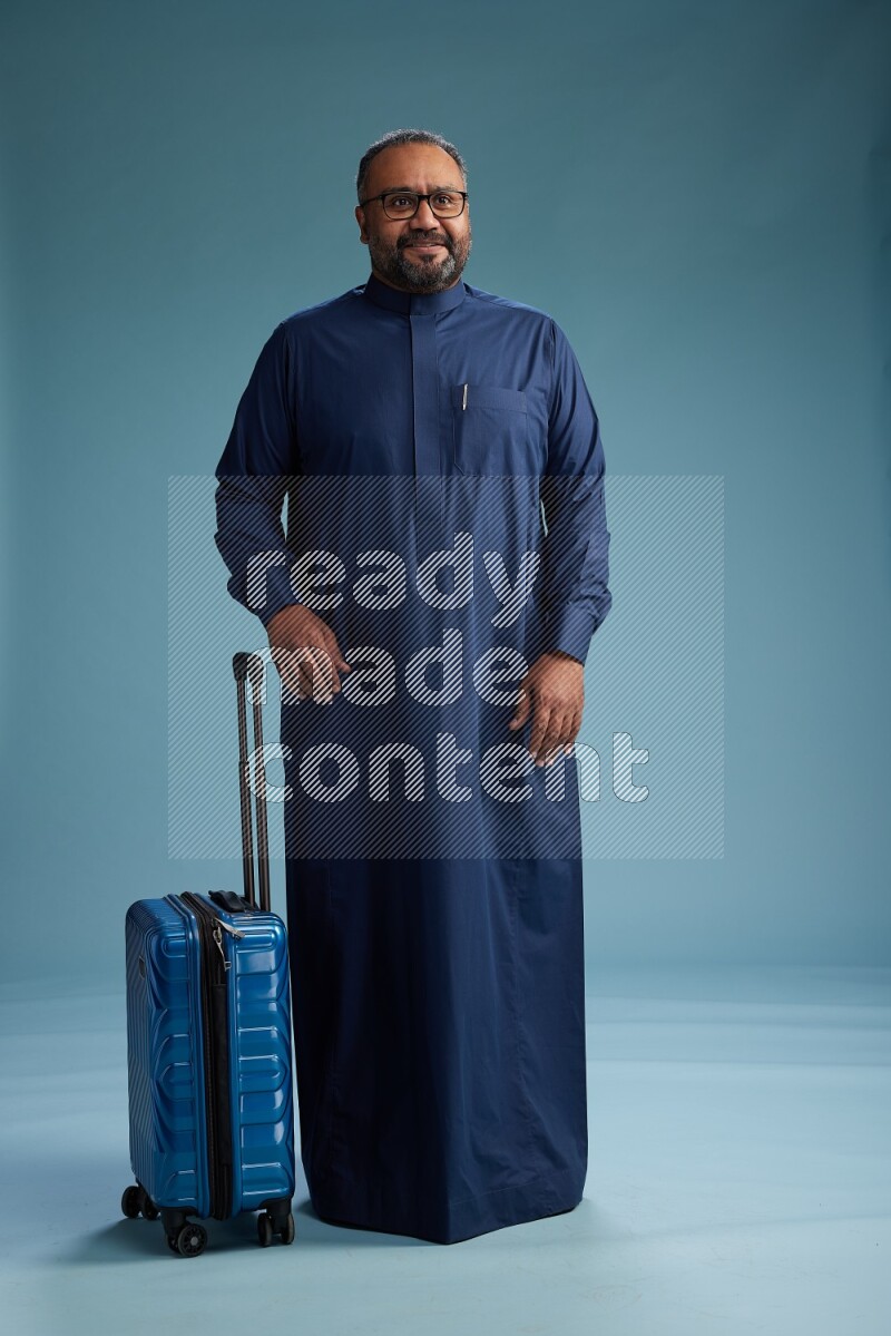 Saudi Man without shimag Standing pulling travel bag on blue background