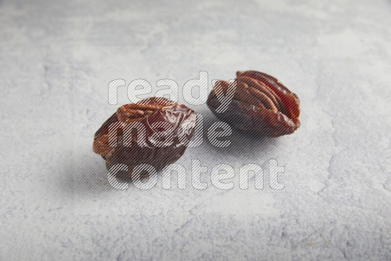 two pecan stuffed madjoul dates on a light grey background