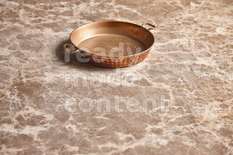 A small copper pan on beige marble background