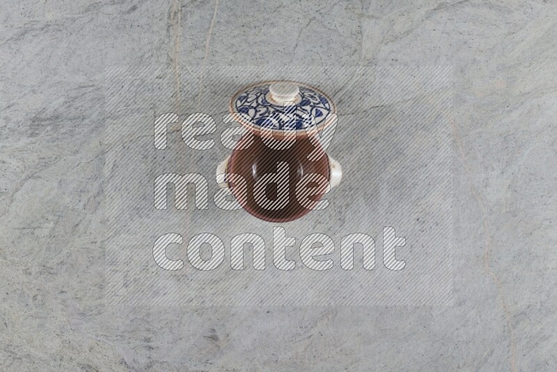 A multicolored pottery pot with its lid on grey marble background