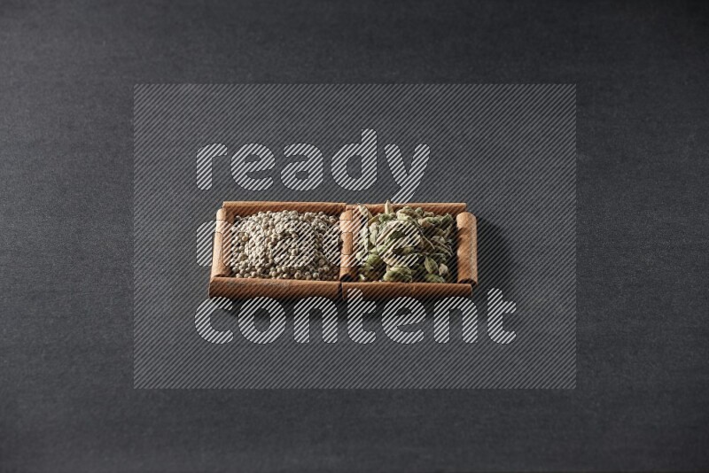 2 squares of cinnamon sticks full of white peppers and cardamom on black flooring