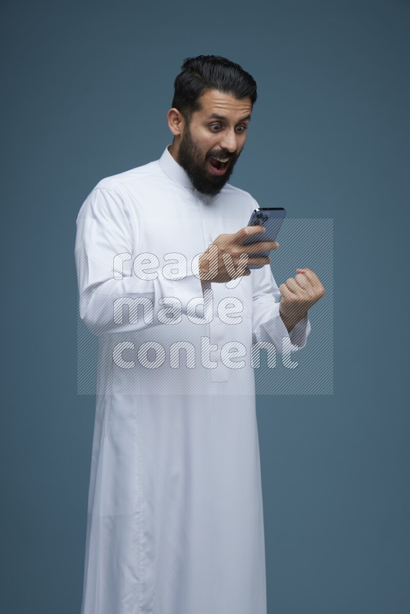 A man Texting in a blue background wearing Saudi Thob