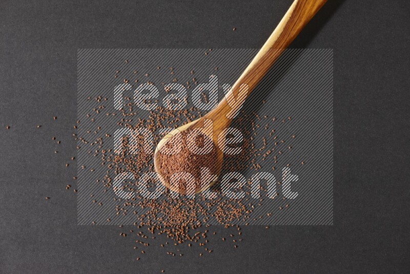A wooden ladle full of garden cress seeds and seeds spread beside it on a black flooring