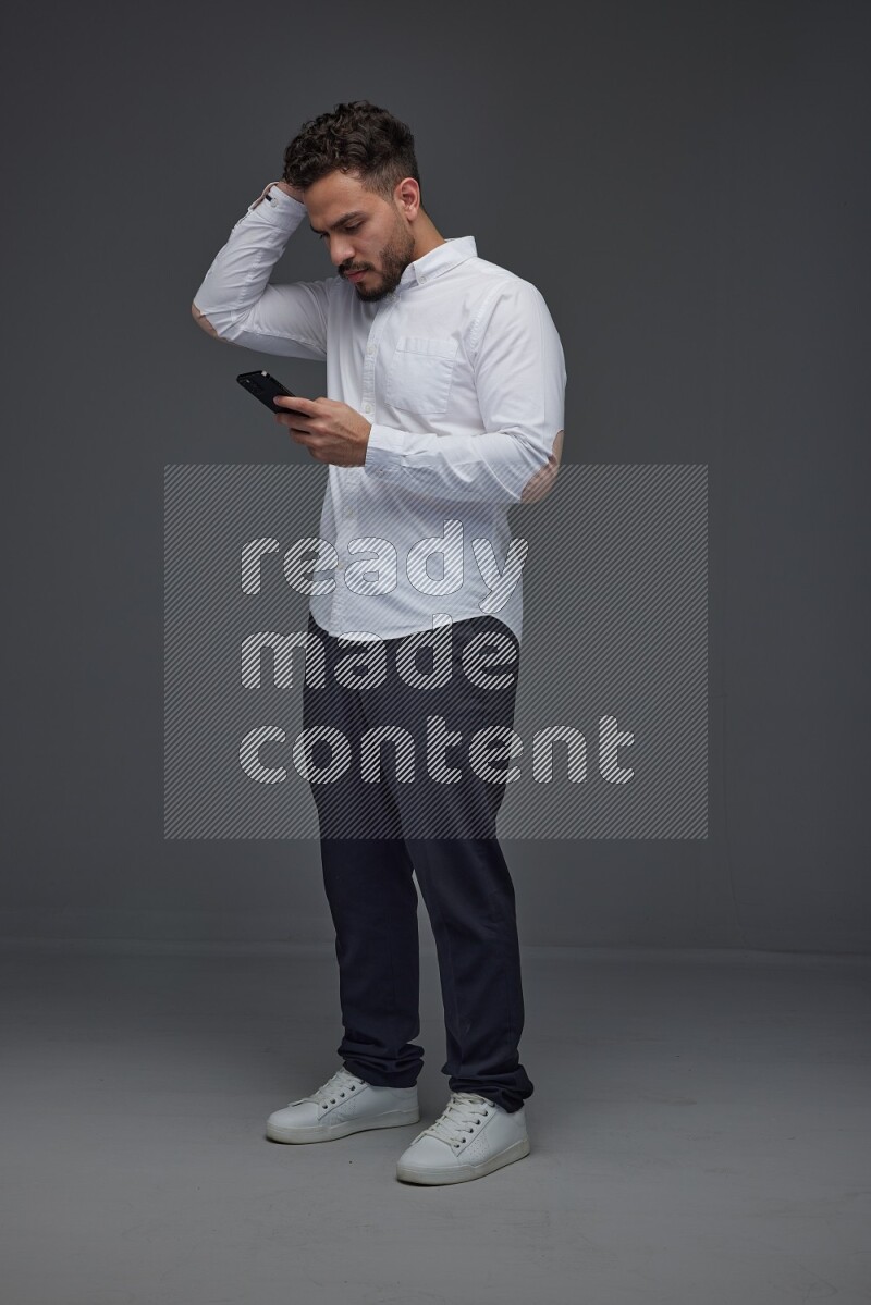A man wearing smart casual standing and using his phone eye level on a gray background