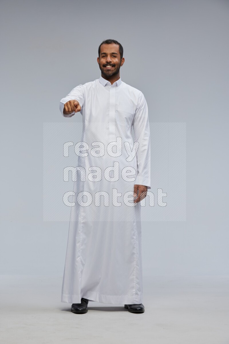 Saudi man Wearing Thob standing interacting with the camera on Gray background