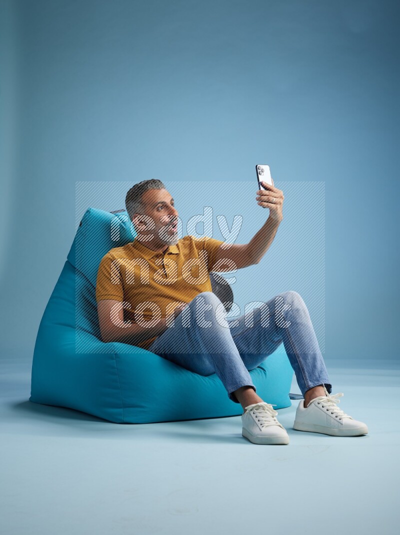 A man sitting on a blue beanbag and taking selfie