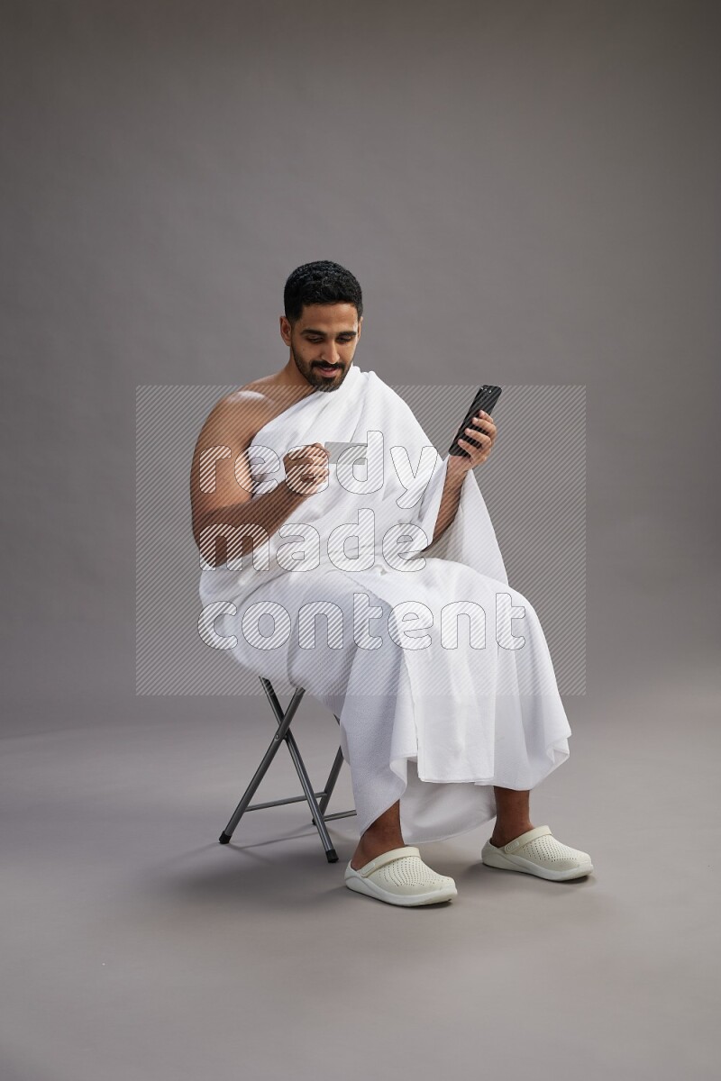 A man wearing Ehram sitting on chair holding ATM card on gray background