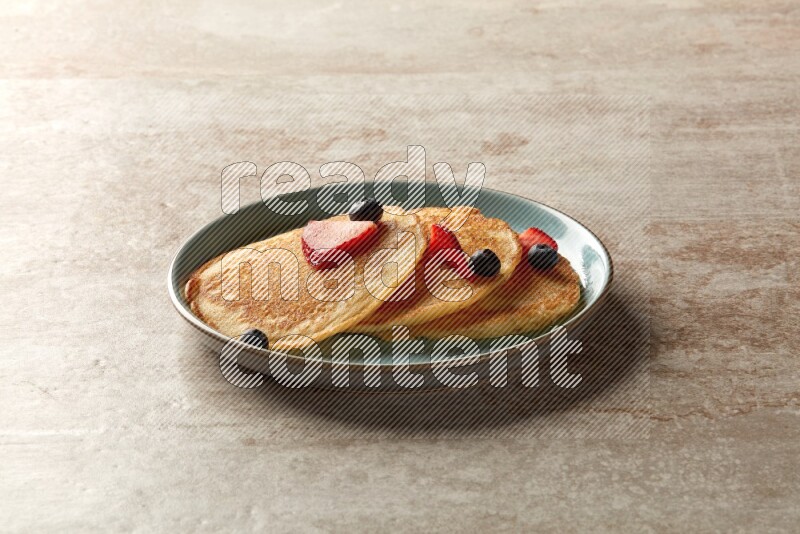 Three stacked mixed berries pancakes in a blue plate on beige background