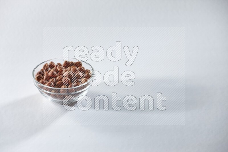 A glass bowl full of peeled hazelnuts on a white background in different angles
