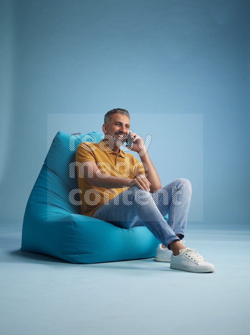 A man sitting on a blue beanbag and talking on the phone