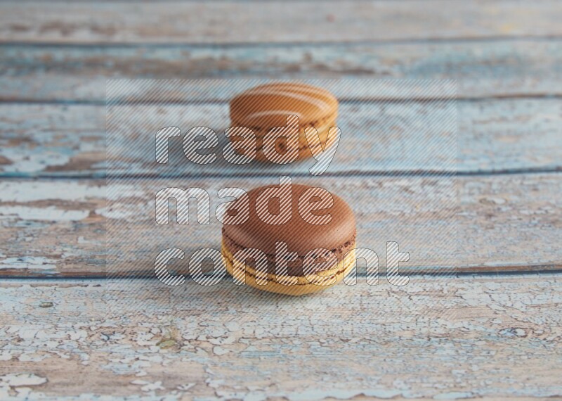 45º Shot of of two assorted Brown Irish Cream, and Yellow, and Brown Chai Latte macarons  on light blue background