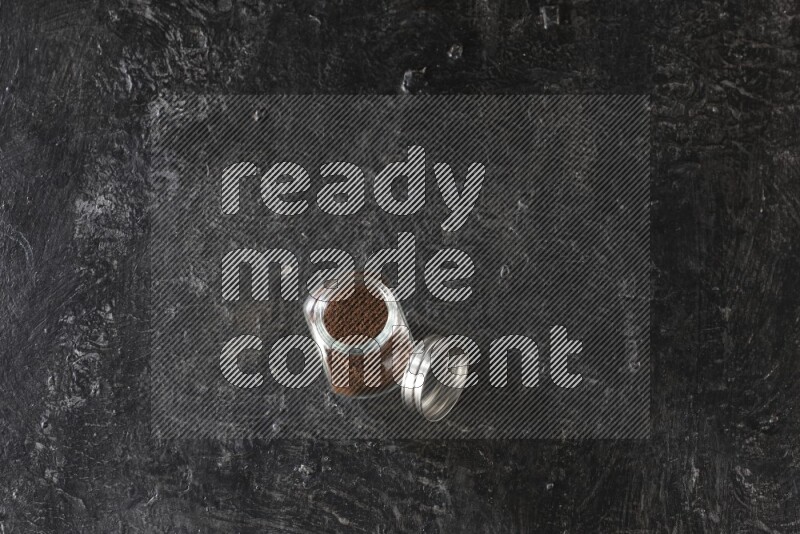 وعاء بهارات زجاجي ممتلئ ببودرة القرنفل على أرضية سوداء