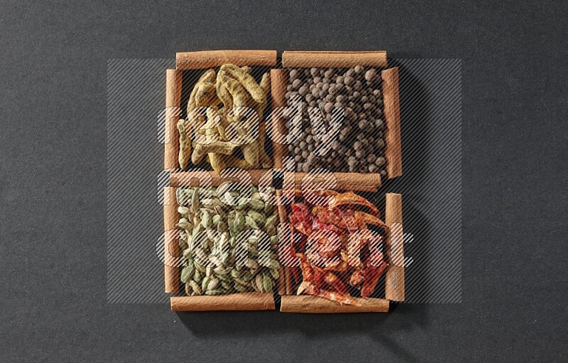 4 squares of cinnamon sticks full of cardamom, dried red chilis, allspice and turmeric fingers on black flooring