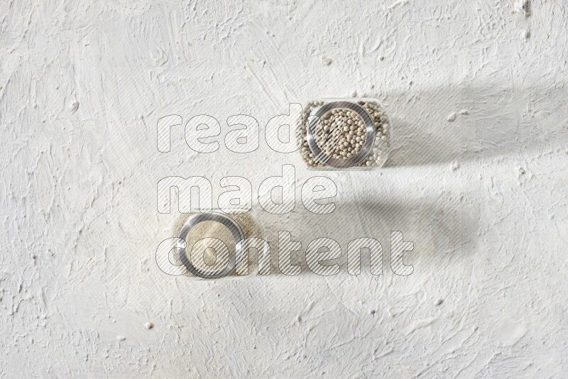 2 Herbal Glass jar full of white pepper beads and powder on textured white flooring