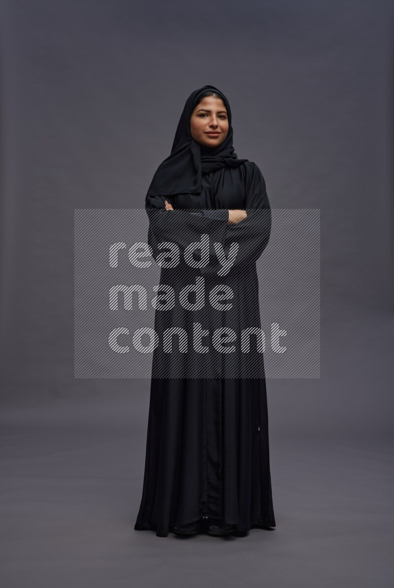 Saudi woman wearing Abaya standing with crossed arms on gray background