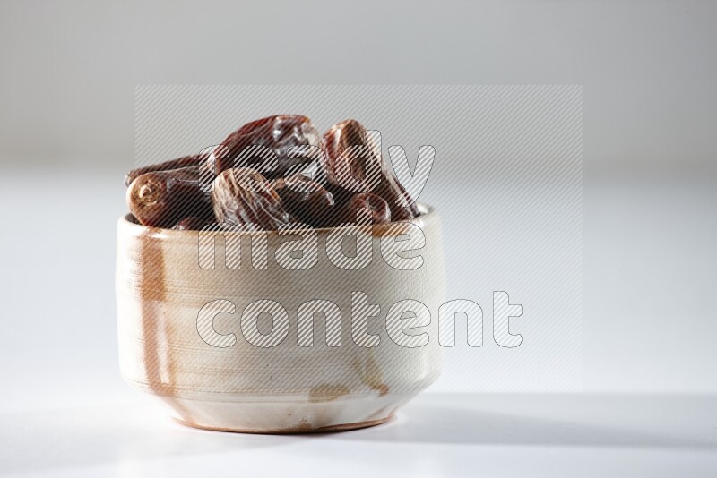 A beige ceramic bowl full of dried dates on a white background in different angles