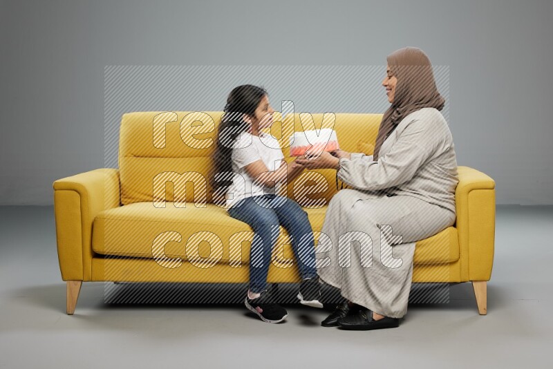 A girl sitting giving a cake to her mother on gray background