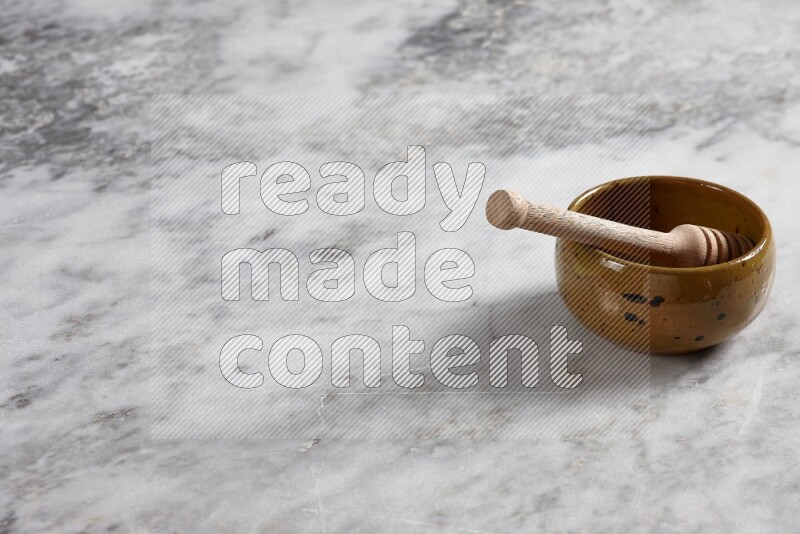 Multicolored pottery bowl with wooden honey dipper in it on grey marble background