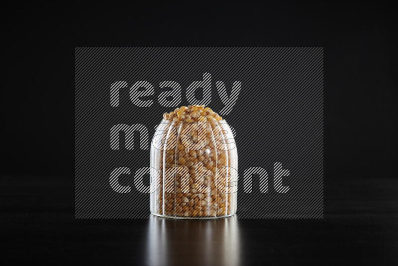 Dry corn kernels in a glass jar on black background