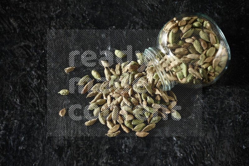 وعاء زجاجي للتوابل مقلوب ممتلئ بحبوب الهيل على خلفية سوداء