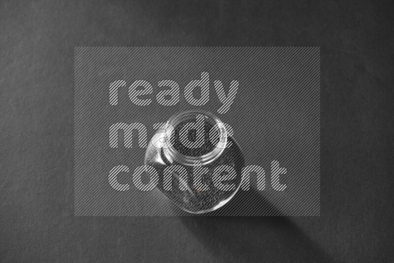 A glass spice jar full of black seeds on black flooring