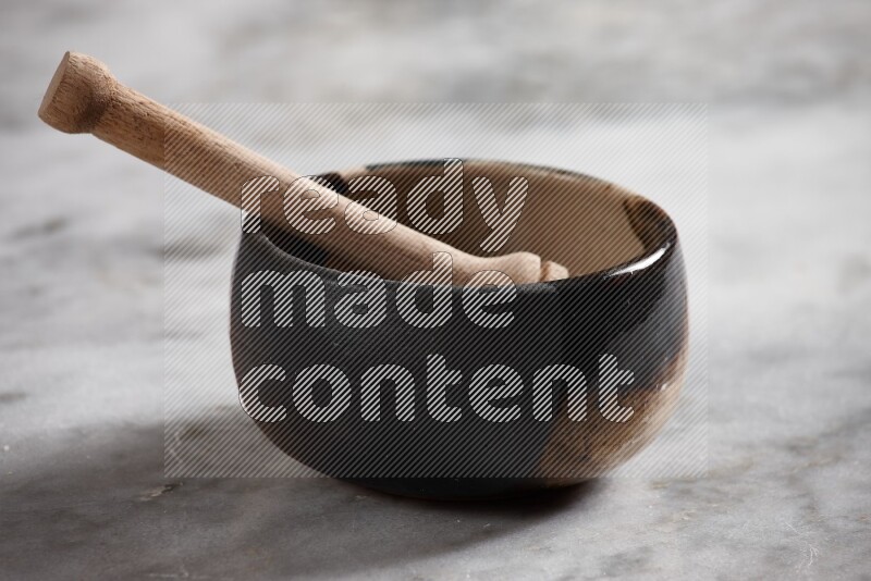 Multicolored pottery bowl with wooden honey dipper in it on grey marble background