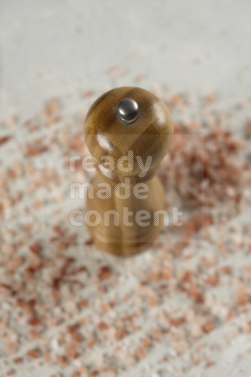 A wooden grinder standing upright and surrounded by coarse pink himalayan salt on white background