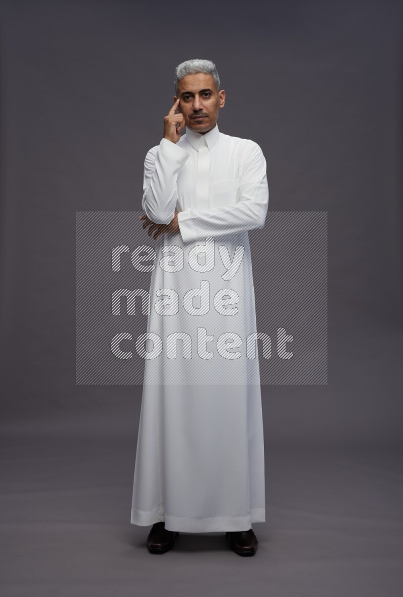 Saudi man wearing thob standing interacting with the camera on gray background
