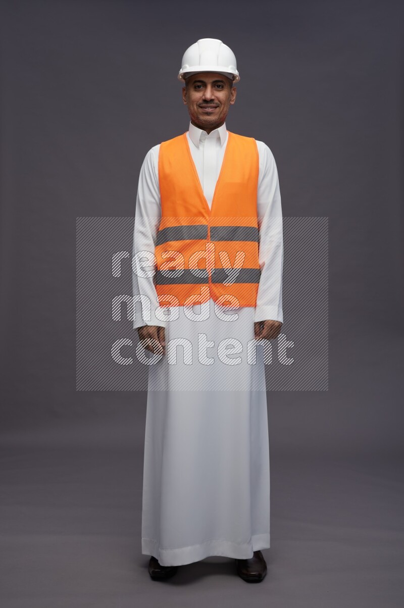 Saudi man wearing thob with engineer vest standing interacting with the camera on gray background